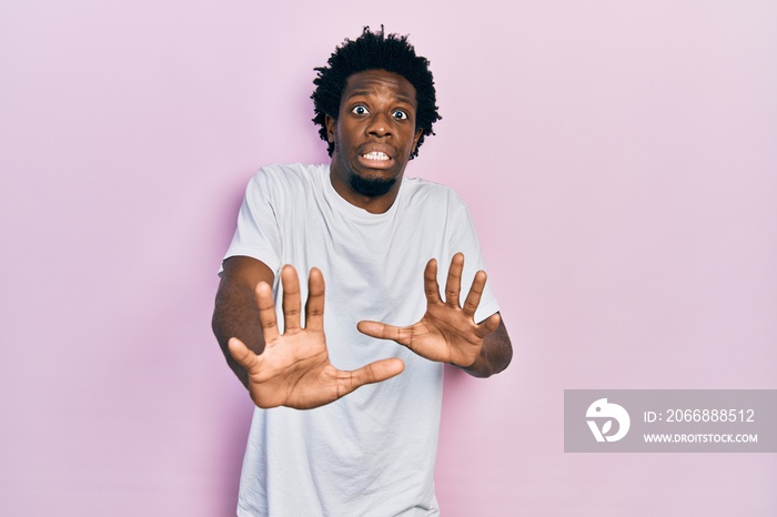 Young african american man wearing casual white t shirt afraid and terrified with fear expression stop gesture with hands, shouting in shock. panic concept.