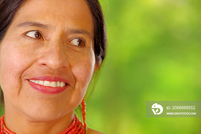 Closeup beautiful hispanic woman wearing traditional andean white blouse with colorful decoration around neck, matching red necklace and ear, posing happily for camera, garden background