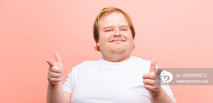 young big size man feeling happy, cool, satisfied, relaxed and successful, pointing at camera, choosing you against pink wall