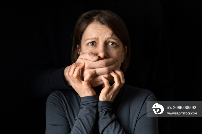 Violence concept. A man’s hand closes a woman’s mouth.