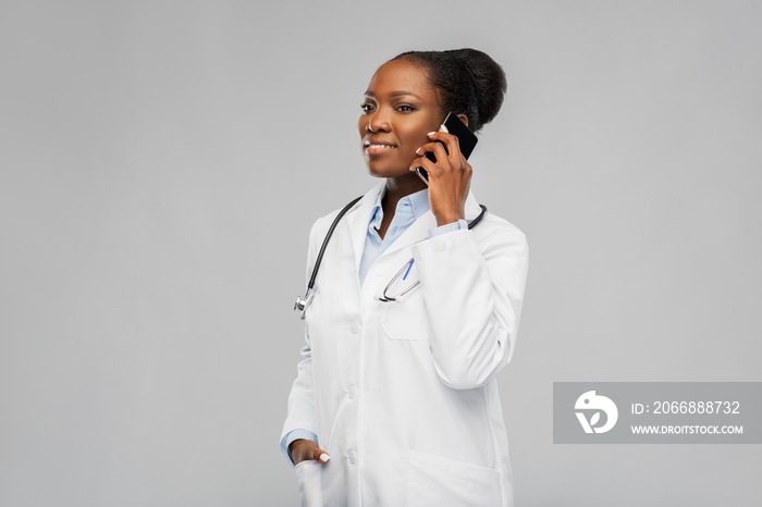 medicine, technology and healthcare concept - happy smiling african american female doctor or in white coat with stethoscope calling on smartphone over background