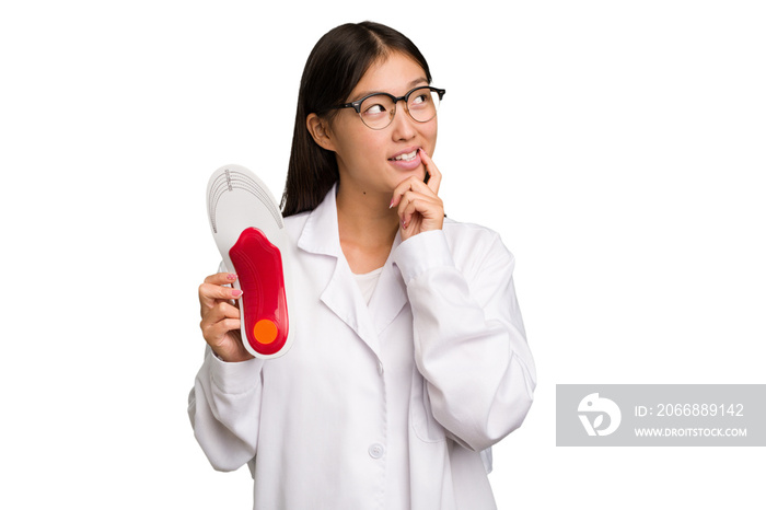 Young asian chiropodist holding a insoles for shoes isolated relaxed thinking about something looking at a copy space.