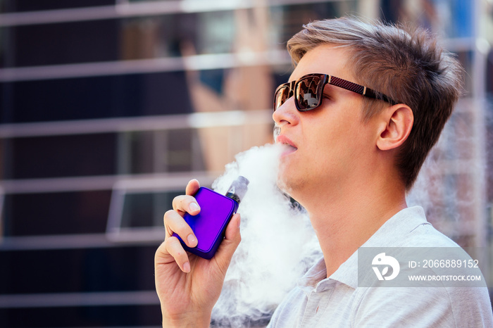 young handsome man in a white shirt smokes a vape on a modern background