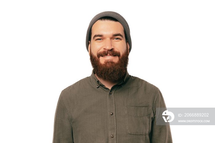 Portrait of young bearded smiling man looking confident at the camera over white backgorund wearing hat.