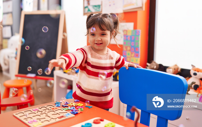 Adorable hispanic girl smiling confident playing with bubbles at kindergarten