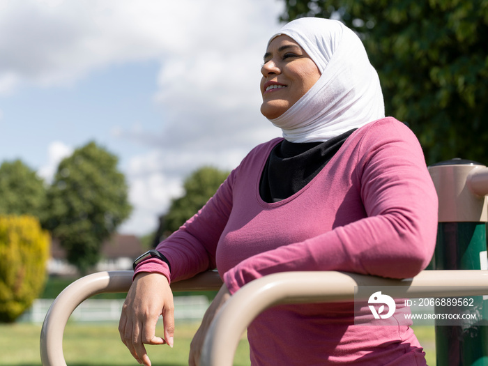 UK,Sutton,Smiling woman in headscarf resting at park gym