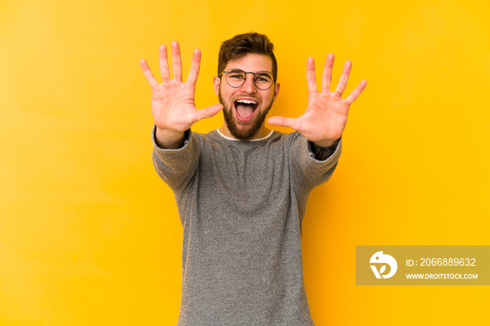 Young caucasian man isolated on yellow background showing number ten with hands.