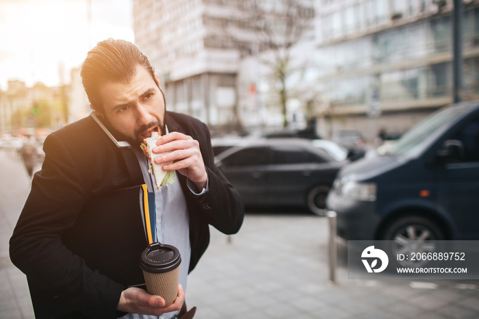 Busy man is in a hurry, he does not have time, he is going to eat snack on the go. Worker eating, drinking coffee, talking on the phone, at the same time. Businessman doing multiple tasks