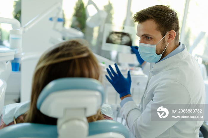 Photo of male dentist showing at patient’s X-ray image in dental office.