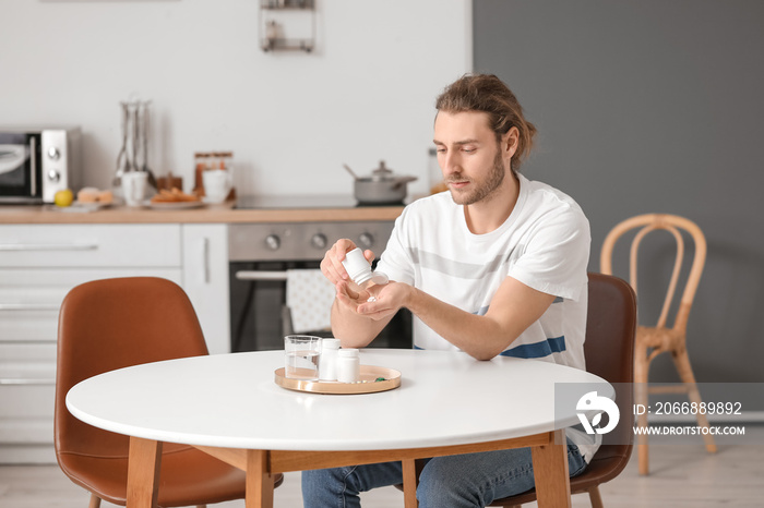 Handsome young man taking pills in kitchen