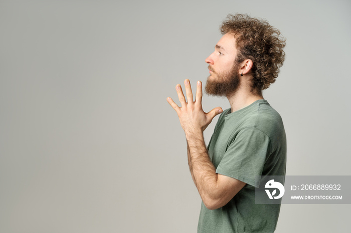 Young handsome man casual sideways pose with palms folded. Handsome young man with curly hair in olive t-shirt looking at camera isolated on white background.