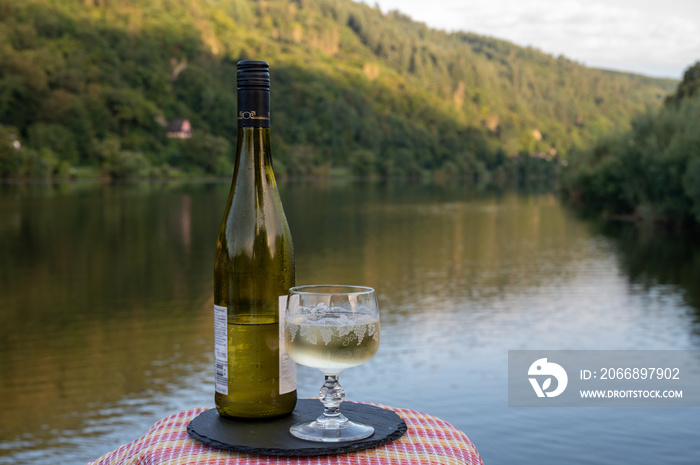 Tasting of white quality riesling wine served on outdoor terrace in Mosel wine region with Mosel river and old German town on background, Germany