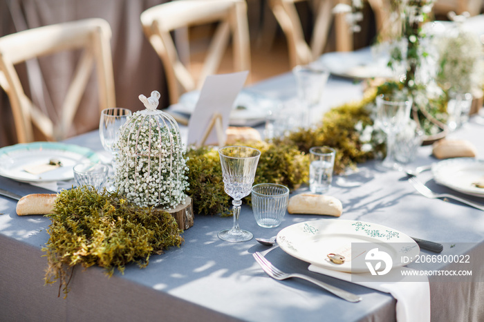 wedding table decorated by plates, knives and forks, candle, moss and greenery