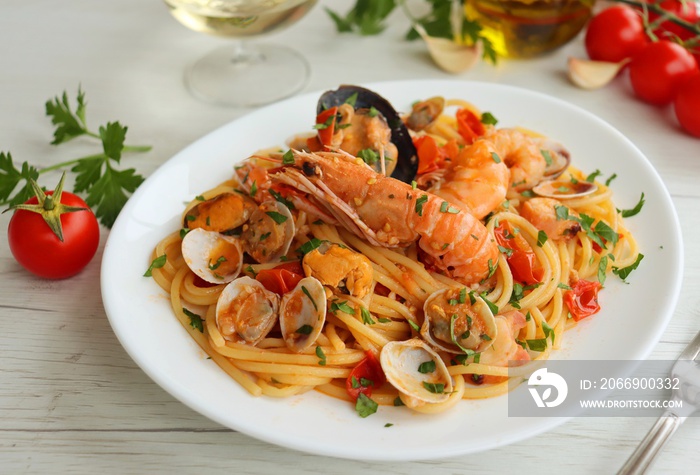 Italian Traditional Dish Spaghetti allo Scoglio  or  Spaghetti with Seafood , spaghetti with mixed seafood,olive oil,garlics,white wine,cherry tomatoes,parsley and peppers on white plate