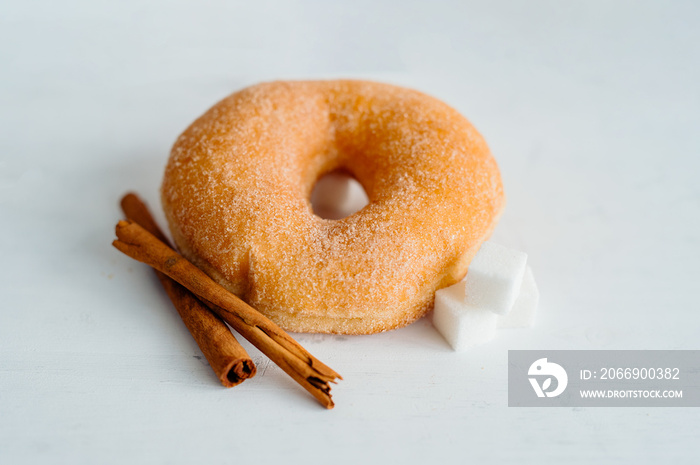 A fried cinnamon and sugar donut on a white background with cinnamon sticks and sugar cubes