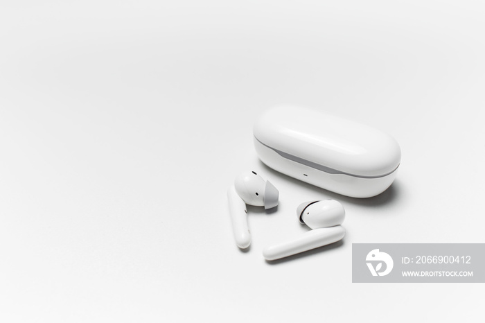 Close-up of wireless earphones lying near closed charging case on white background with copy space.