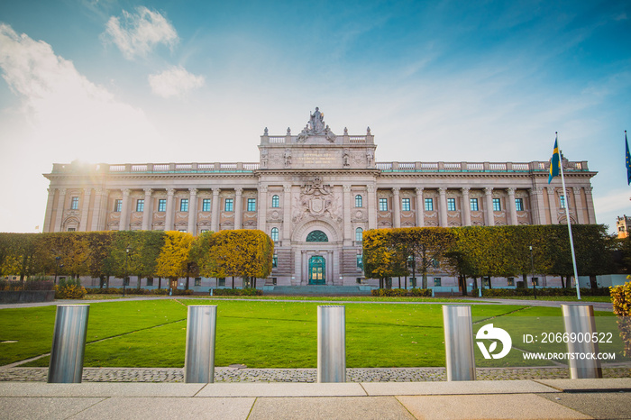 Swedish parliament house Riksdag, with its neoclassical facade in downtown Stockholm on a sunny autumn day. Sun flare visible on top and brown leaves in the foreground of the house