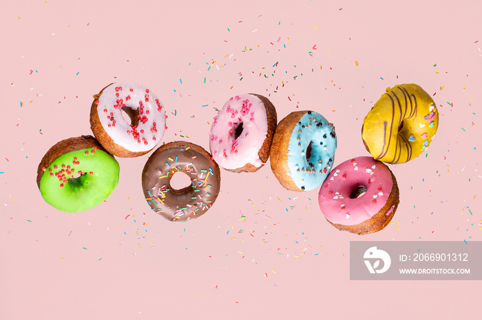 Doughnut collection with flying blue, pink, green and yellow donuts on pink background