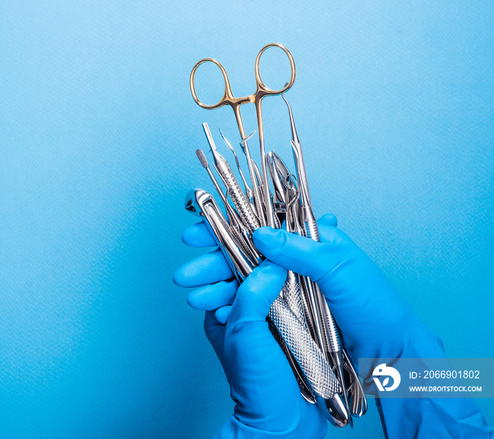 Hand in blue glove holding surgery dental tools on light blue background