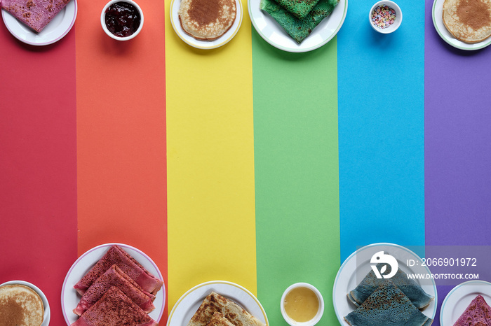 Rainbow pancakes, different color crepes. Spinach, beetroot powder, blue matcha and turmeric crepes. Colorful pancakes, flat lay on rainbow layered paper. Copy-space, text space