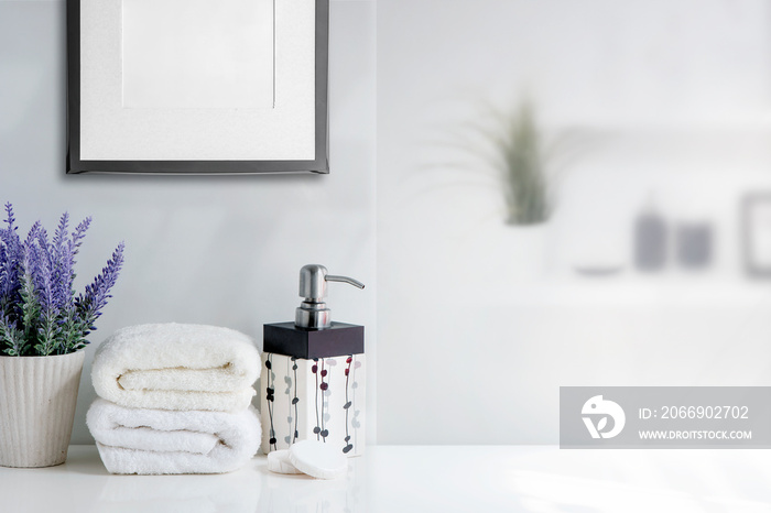 Mockup bath towel with liquid soap bottle and houseplant on white table in white room.