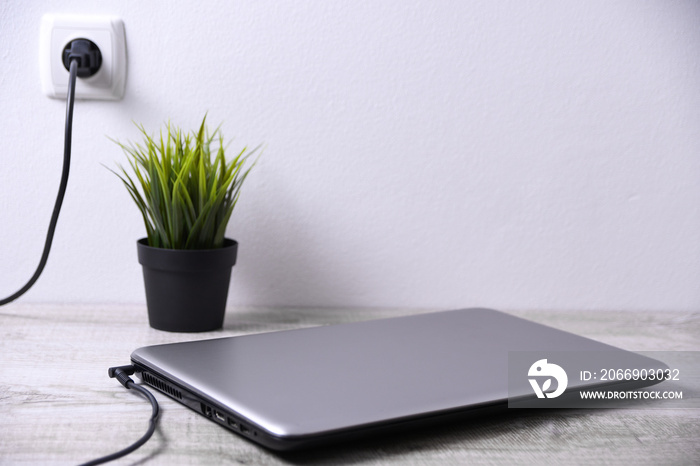 Laptop, computer is charging from a 220-volt outlet on a desk near the wall. Energy, accumulation. Mockup