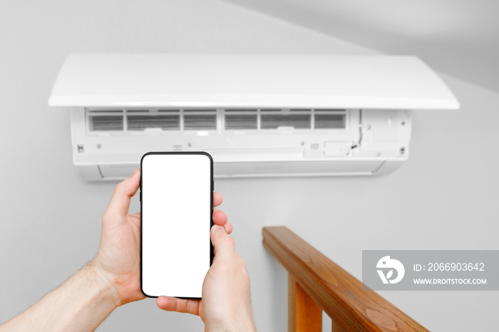 A male technician holds a mobile phone in his hands using a blank white screen mockup. Smart diagnostics of the air conditioner by phone.