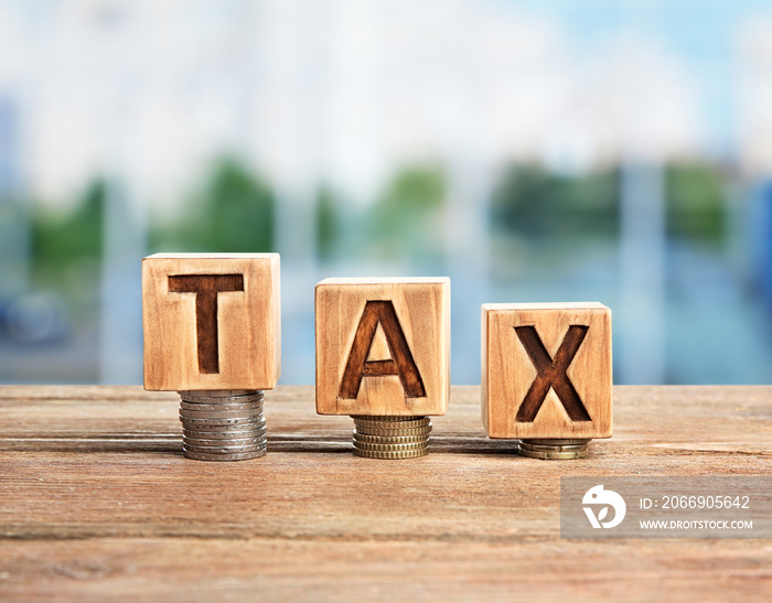 Word tax on wooden blocks with stacked coins. Financial concept.