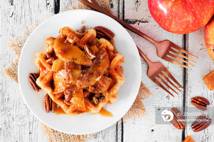 Sweet breakfast waffle with baked apple, pecans and caramel. Top view over a white wood background. Autumn food theme.