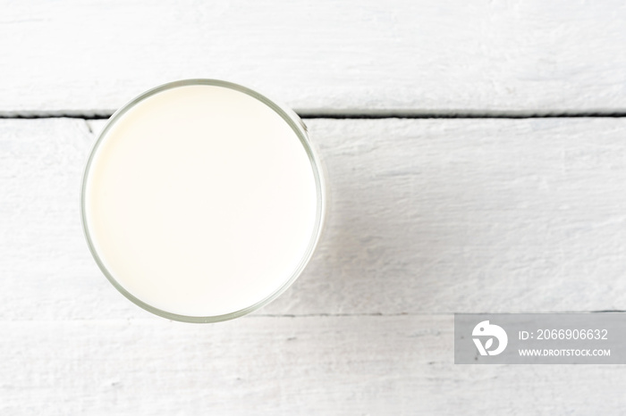 Overhead shot of glass of milk on white wooden table. Close up