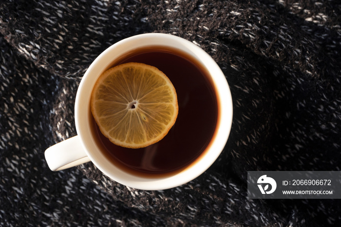 Close-up black tea with lemon slice in white cup on background from knitted sweater, horizontal. Hot drink, above