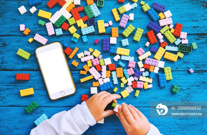 Child playing hands with colorful plastic blocks and mobile phone