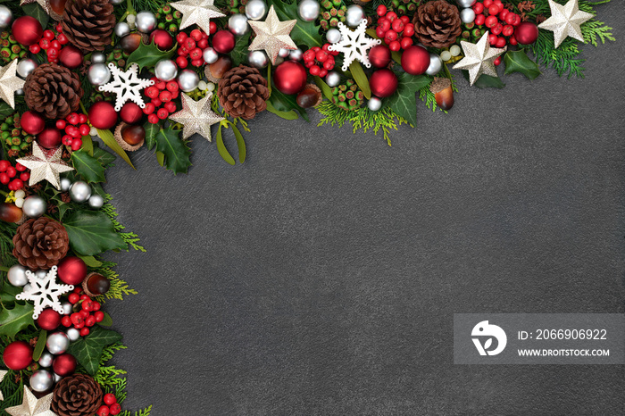 Festive Christmas background border with star and ball baubles, holly, mistletoe and winter flora on grunge grey background with copy space.