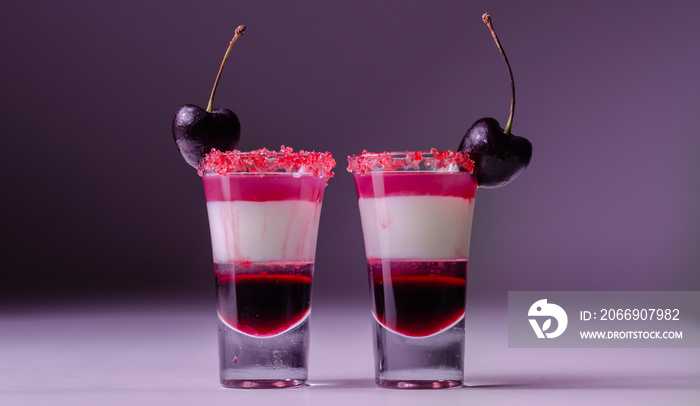 Three-layer cocktail based on vodka, cherry liqueur and syrup in drink shot glass, decorated with fresh cherry and red sugar