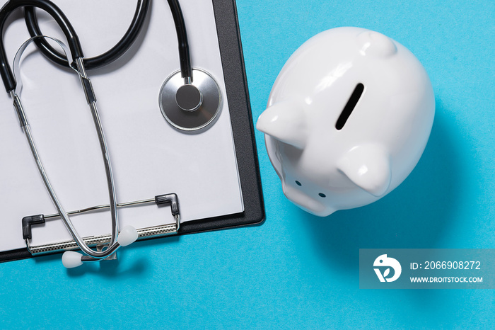 Creative composition with clipboard, medical stethoscope and piggy bank on bright blue background. Concept of medical insurance and private medicine.