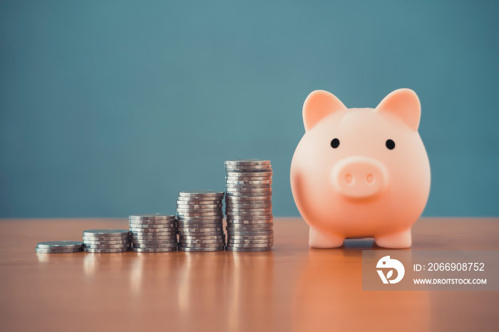 pink piggy bank and money stack tower on a wooden office desk table with blurred blue background conceptual for business finance