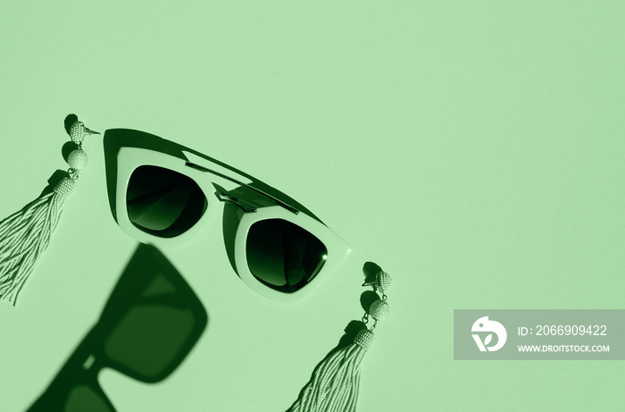 Composition made with woman accessories. Sunglasses and earrings on pastel green background.