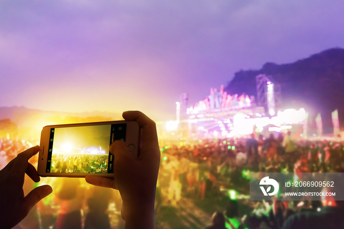 Silhouette hand with a smartphone records live music festival and taking photo of concert stage live concert.