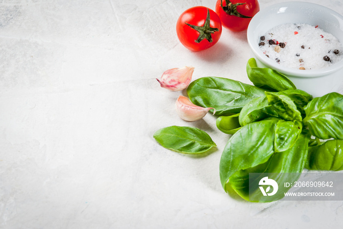 Food background. Ingredients, greens and spices for cooking lunch, lunch. Fresh basil leaves, tomatoes, garlic, onions, salt, pepper. On a white stone table. Copy space