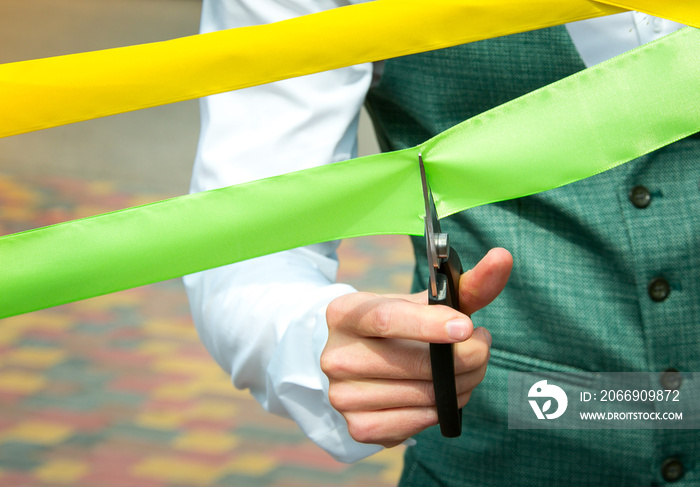The businessman cuts the yellow and green ribbons with scissors. Holiday concept.