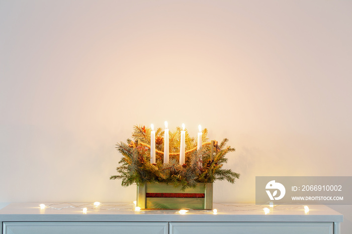 advent decoration with fir branches and four burning candles in wooden basket on white background