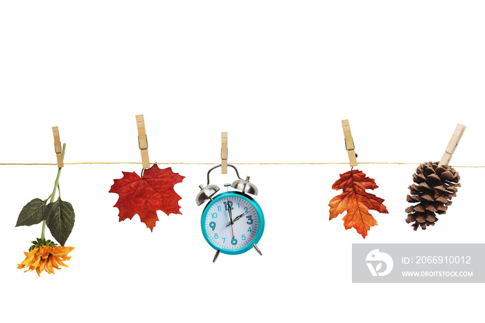 Set your clocks back with this clock, flower, autumn leaves and and pine cone hanging by clothes pins to a clothes line over a white background. Daylight saving time concept. Clipping path included.