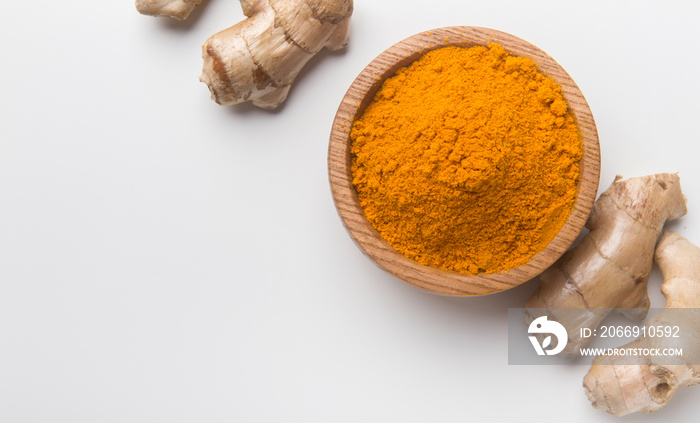 Turmeric powder in a wooden bowl and fresh turmeric root