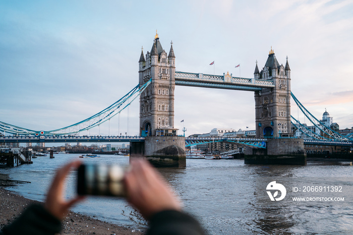 Woman taking a photo with the smart phone to the Tower Bridge in London on a sunny winter day, London, Great Britain.