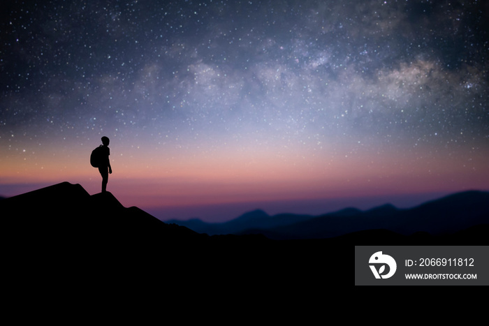 Silhouette of young male traveler with backpack standing and watching the star, milky way over the sky alone on top of the mountain. He enjoyed traveling and was successful when he reached the summit.