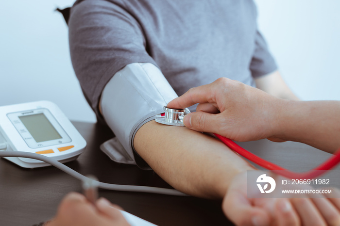 Doctor using sphygmomanometer with stethoscope checking blood pressure to a patient in the hospital.