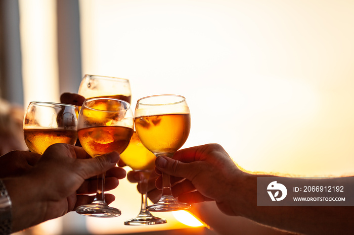 Close-up shot of friends or family raising glasses and toasting with wine against the sunset light during the celebration or party