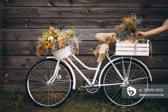 Basket with spring flowers standing on the bicycle by the wooden background