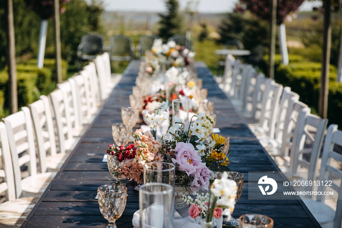 Long wooden table decorated with flowers for an outdoors wedding party.