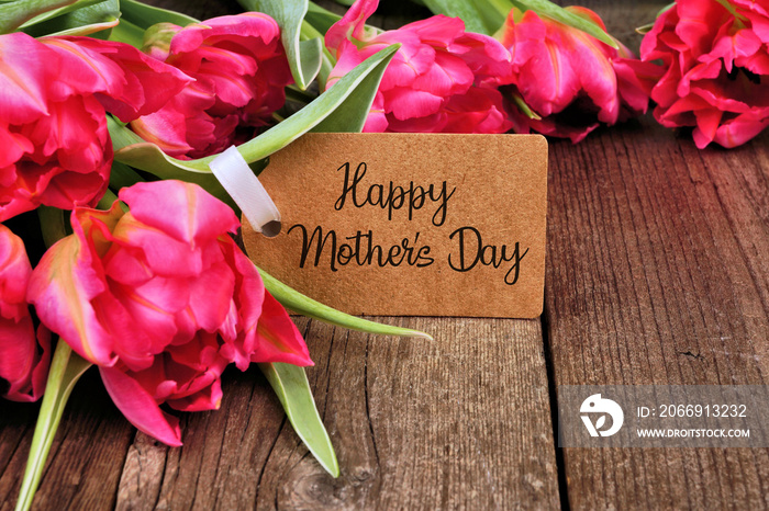 Happy Mothers Day tag close up among a bouquet of pink tulip flowers over a dark wood background